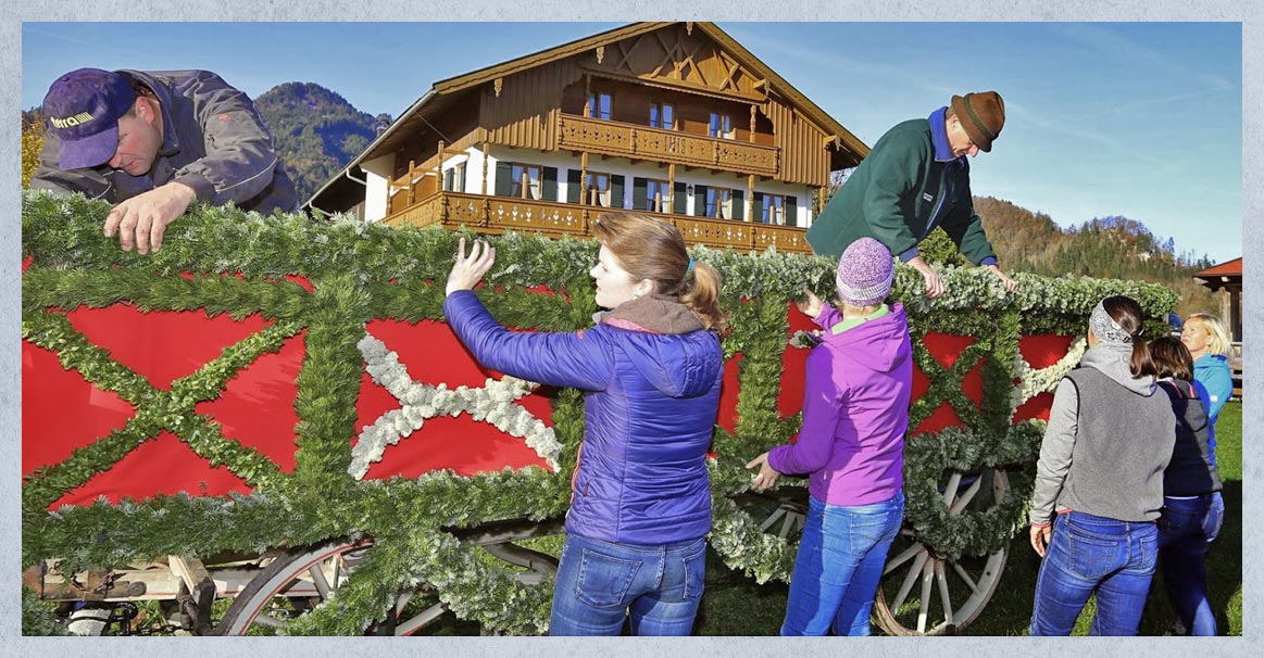 Fünf Frauen und zwei Männer schmücken ein Leonhardi-Fuhrwerk. Im Hintergrund ein großes Bauernhaus.